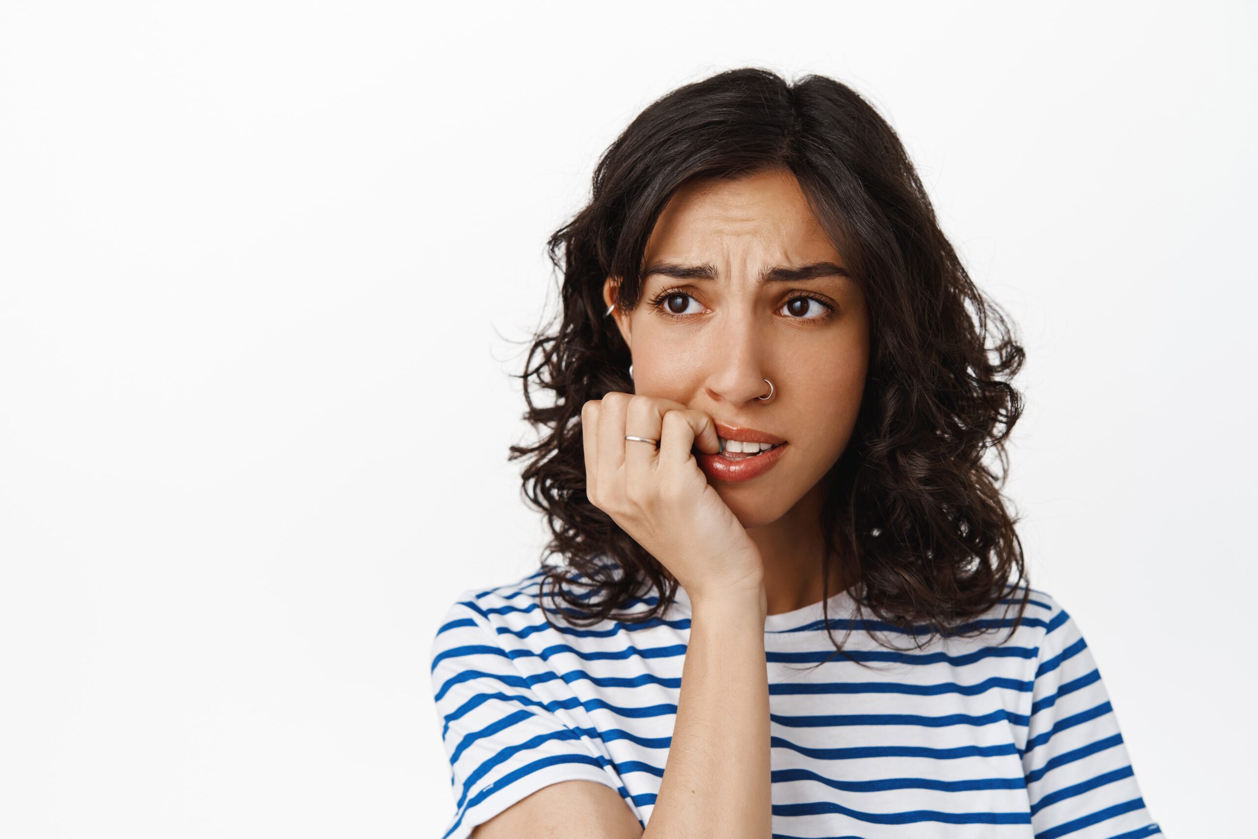 Close up anxious brunette girl biting finger nails looking away with alarmed nervous face feeling scared consequences being afraid standing white min
