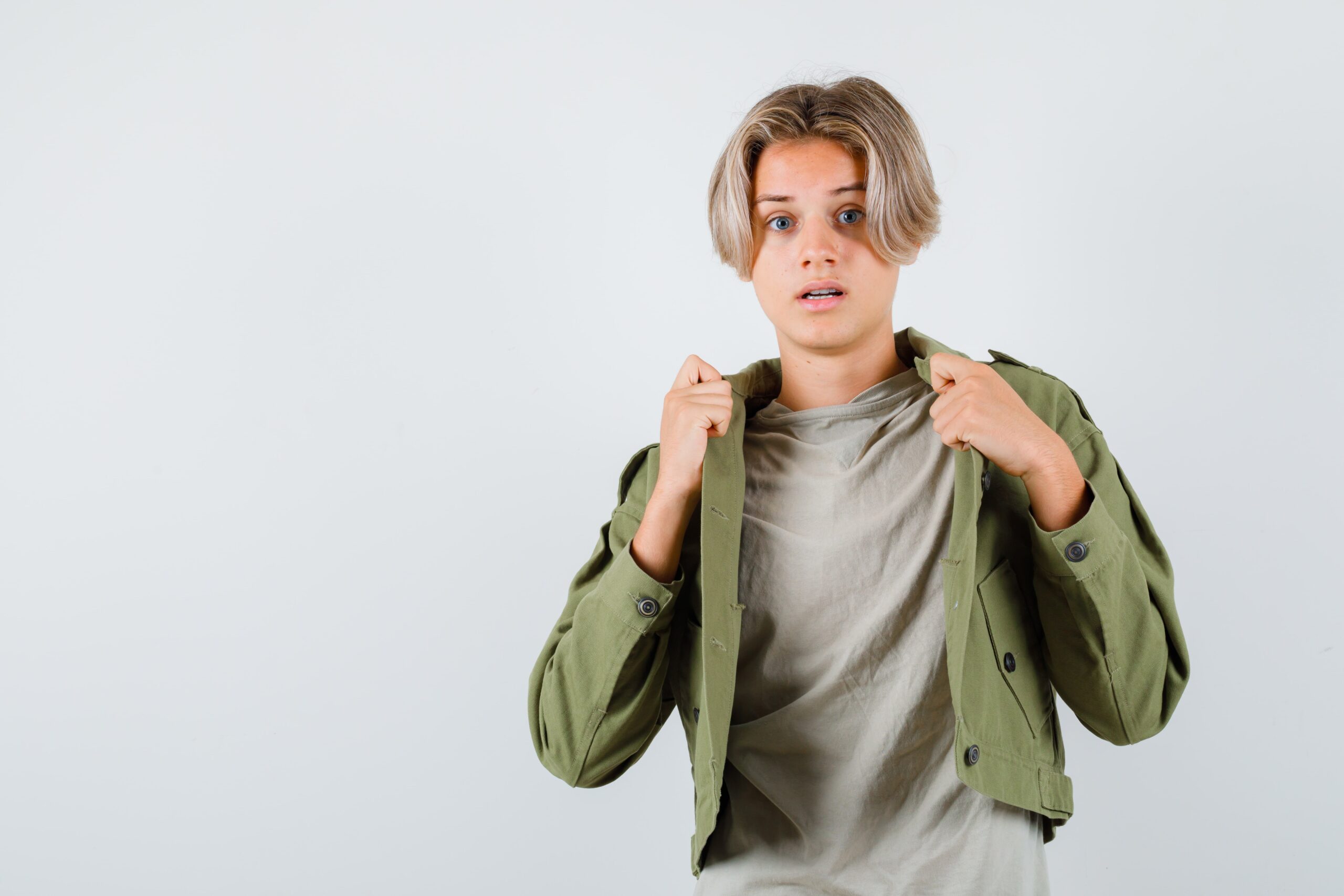 Cute teen boy pulling his open jacket green jacket looking scared front view min